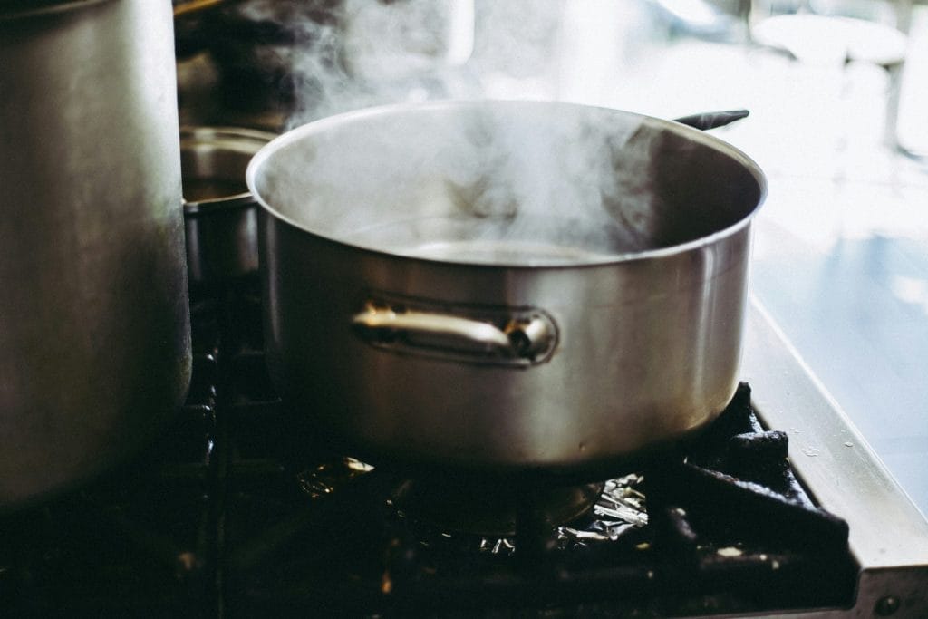 Une casserole en métal bouillante sur une cuisinière à gaz, avec de la vapeur s'élevant de l'eau, dans un décor de cuisine avec un arrière-plan flou.