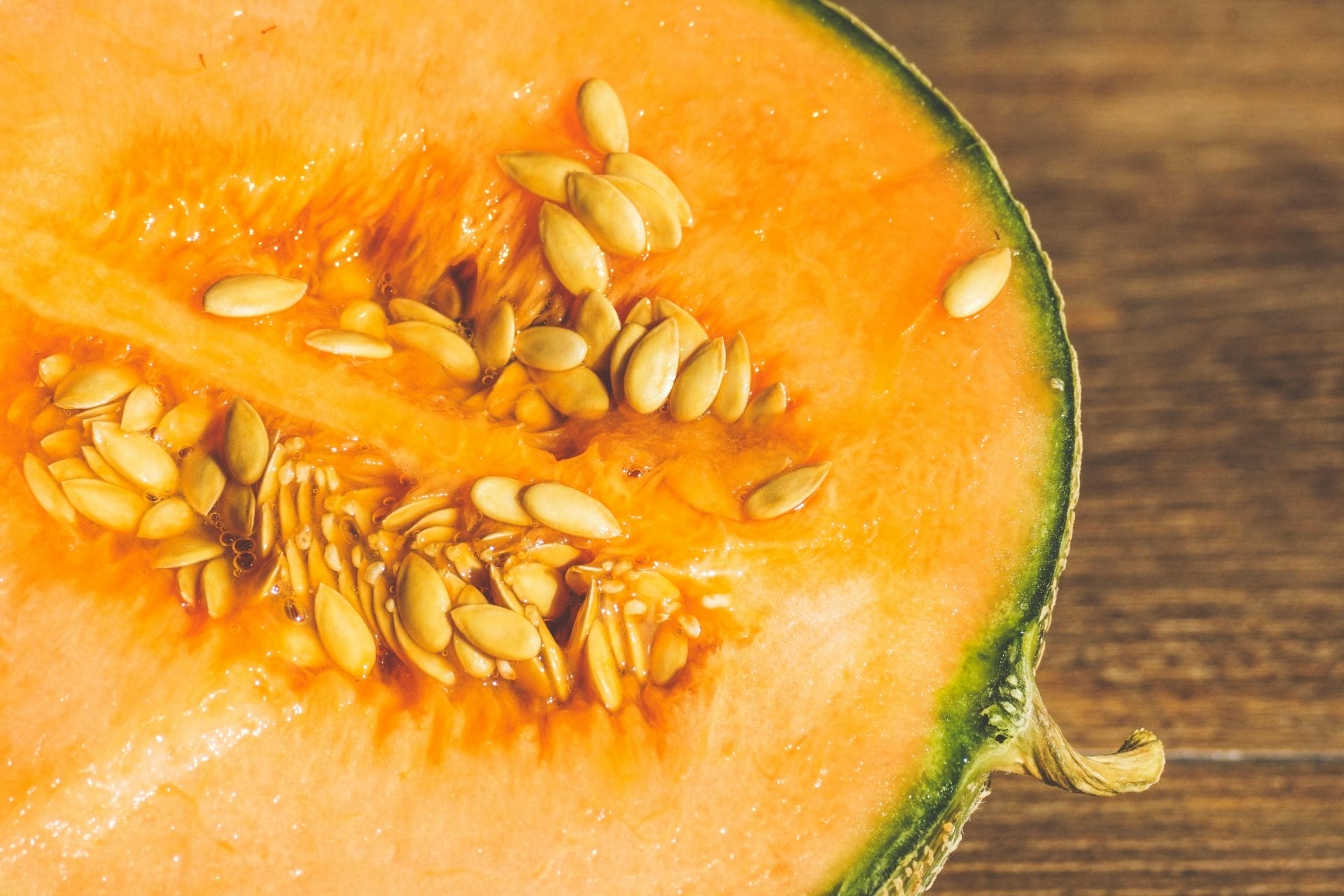 Gros plan d'un melon cantaloup coupé en deux, présentant une chair orange, des graines regroupées au centre et une écorce verte, posé sur une surface en bois.