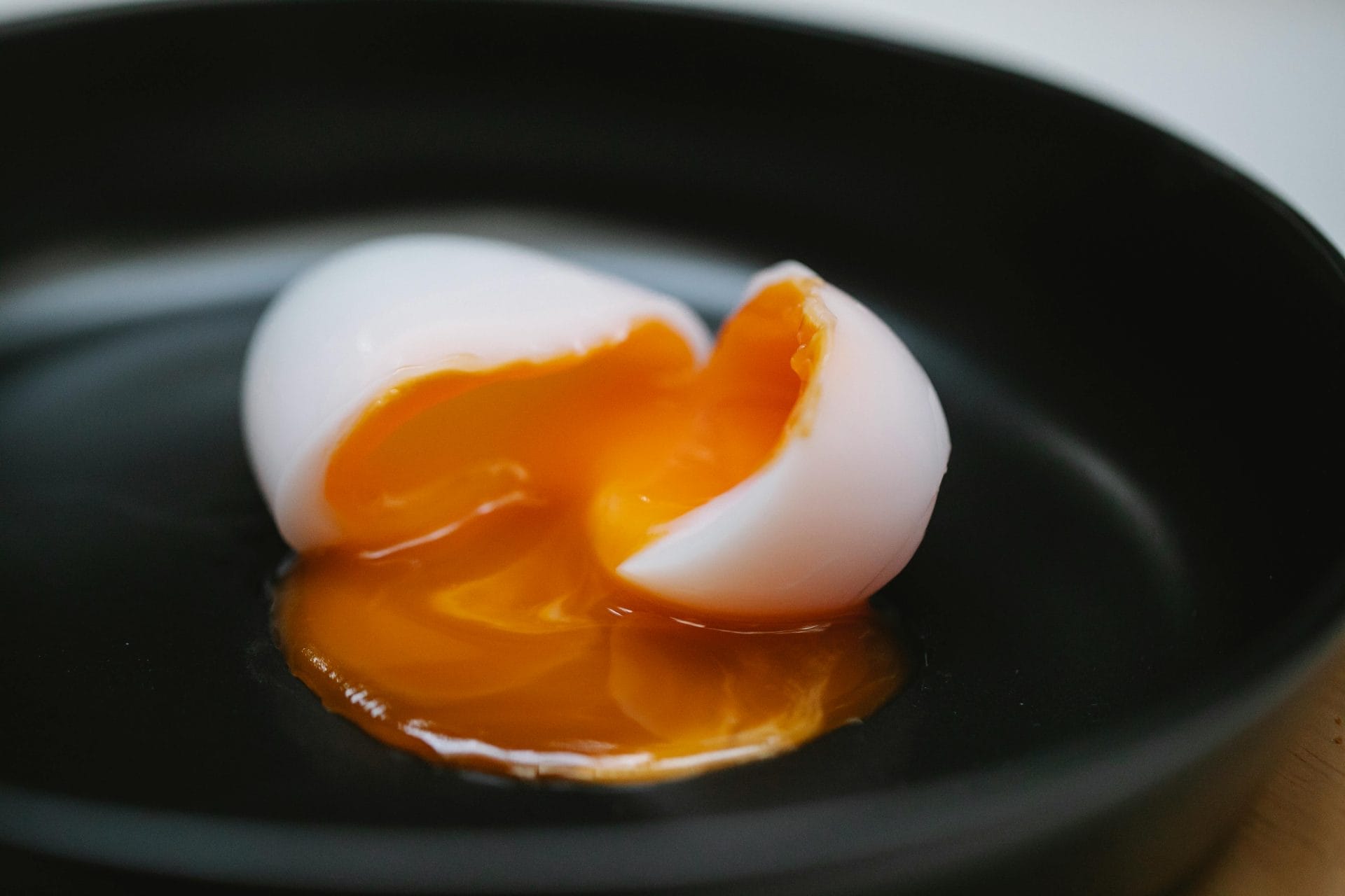Un œuf à la coque au jaune coulant est fendu sur une assiette noire, le jaune se répandant sur l'assiette.