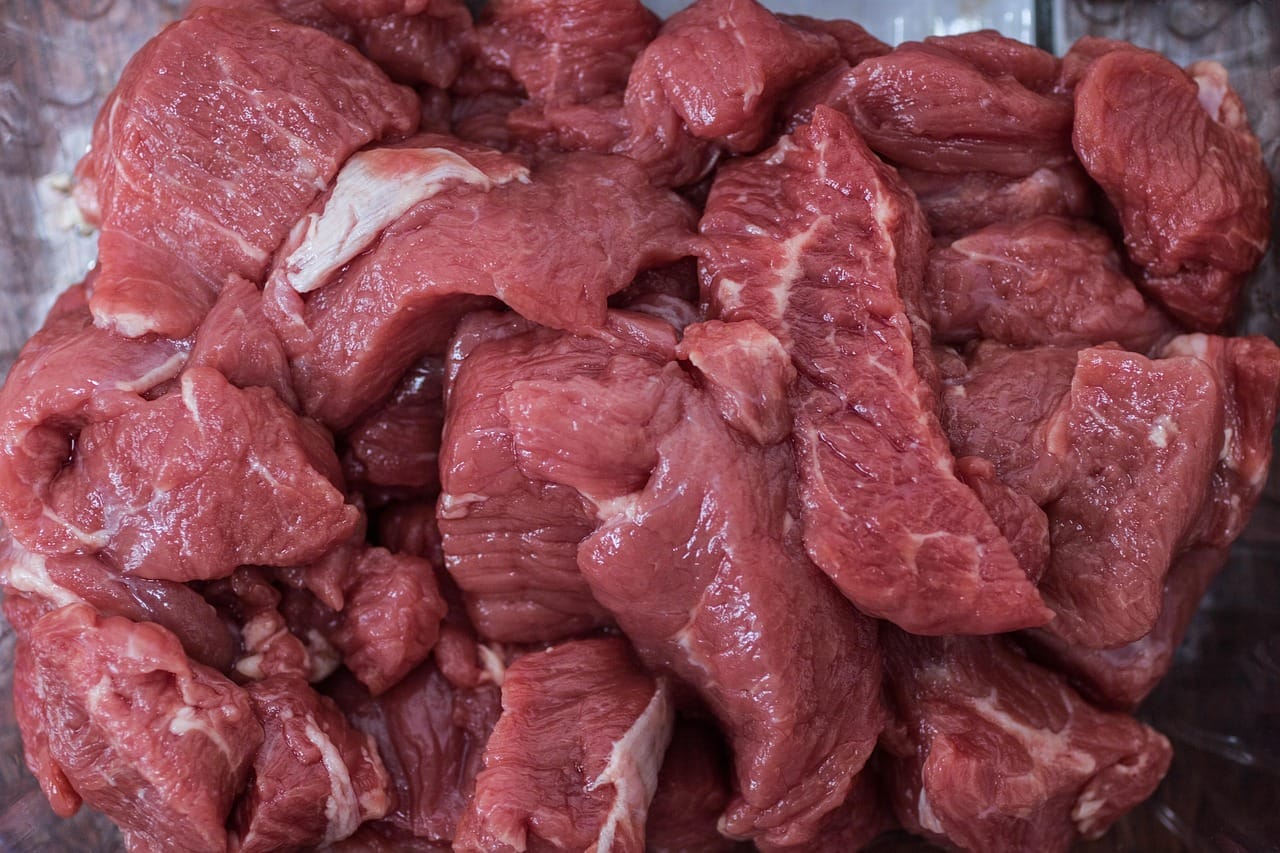 Vue rapprochée de plusieurs morceaux de viande rouge crue empilés, montrant leur texture et leur persillage.